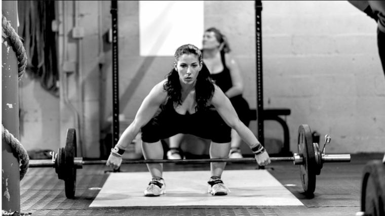 Woman on a lifting platform grabbing a barbell with both hands, prepared to do a snatch