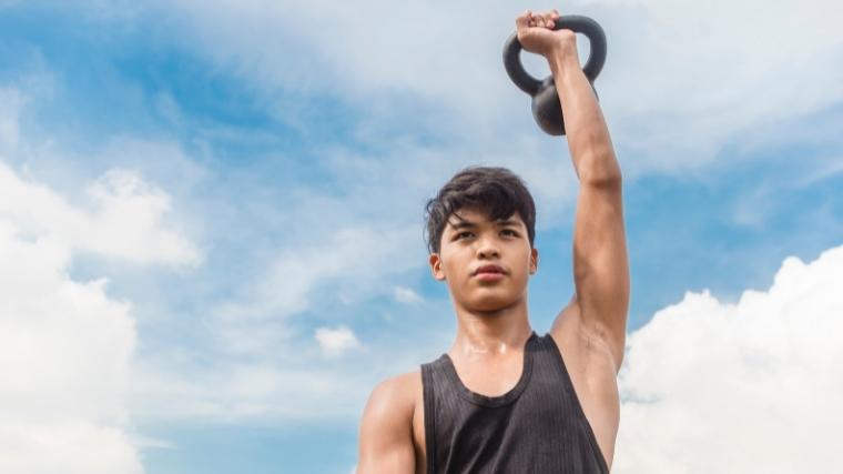 Man pressing a single kettlebell over his head outside