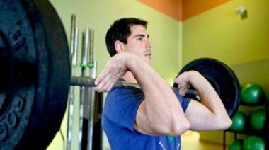 Man holding a barbell laoded with plates in a front-rack position