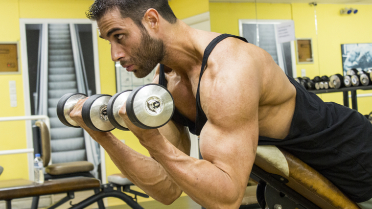 Man in gym leaning on bench curling dumbbells