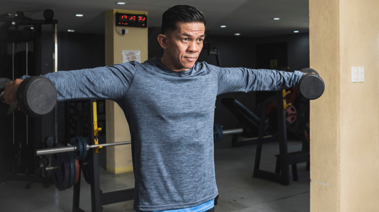 Man in gym performing shoulder exercise with dumbbells