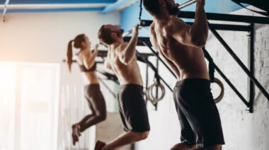 Three people performing pull-ups on wall-mounted bars.