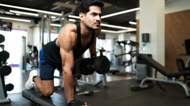 Muscular man in gym rowing dumbbell