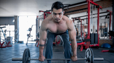 Muscular man in gym holding barbell on groun