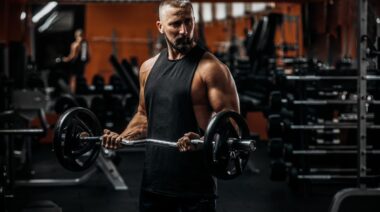 Person wearing a black cut-off t-shirt curling a loaded barbell