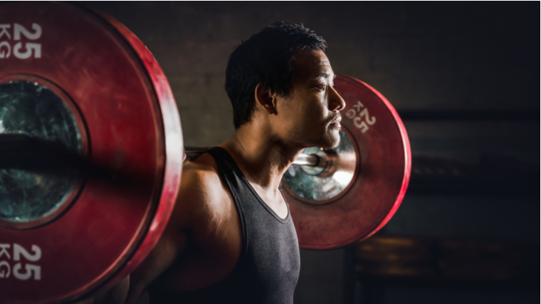 person standing with barbell across shoulders