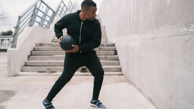 man outdoors throwing medicine ball at wall