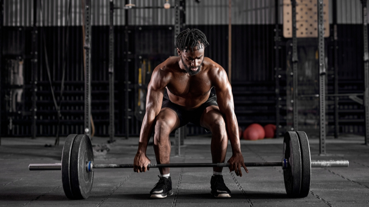 muscular person in gym grabbing barbell on floor