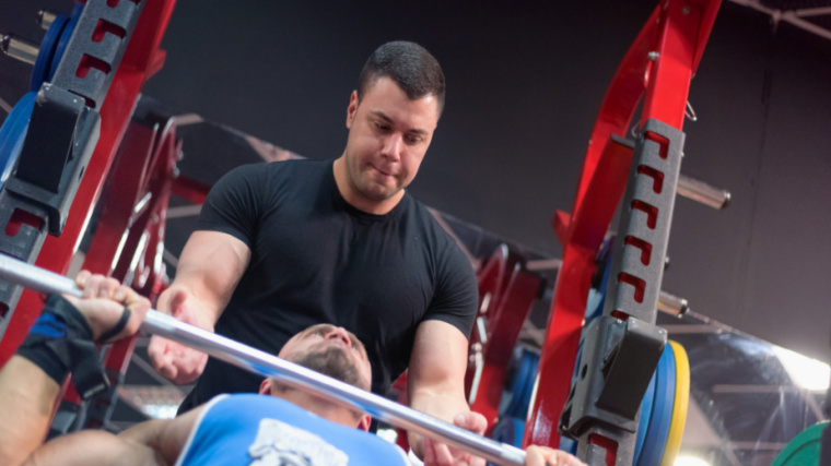 muscular person performing barbell press with spotter