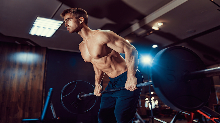 shirtless muscular person performing barbell row in dark gym