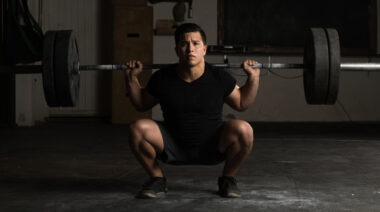 person in dark gym performing deep barbell squat