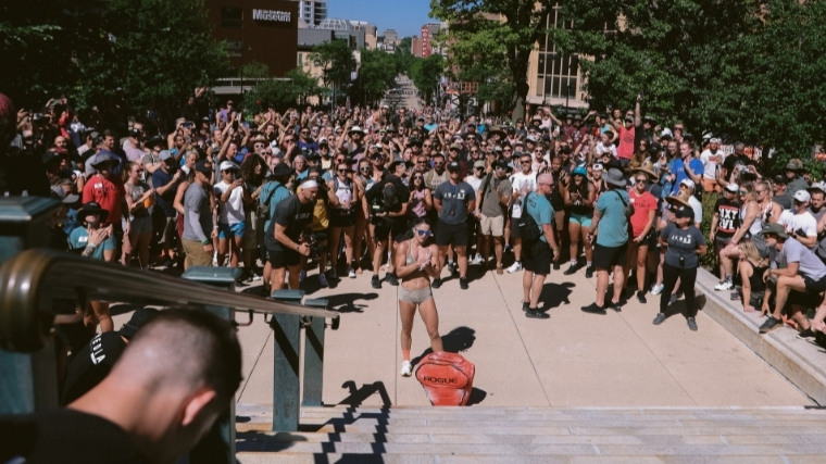 Woman in shorts and sports bra stands in front of a sandbag at foot of the stairs of the Wisconsin Capitol building.