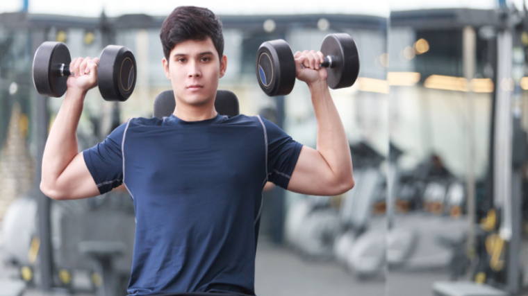 person in gym doing dumbbell shoulder press