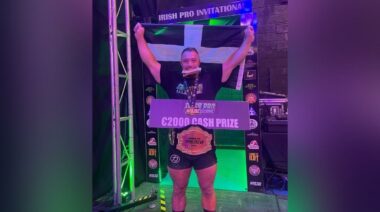 Powerlifter Chris Kugh holding a flag behind him while wearing a belt.