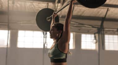 person in gym pressing barbell overhead