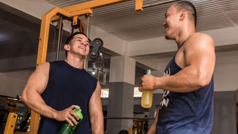 Two muscular people in gym drinking shakes