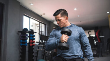 Muscular person in gym curling dumbbell