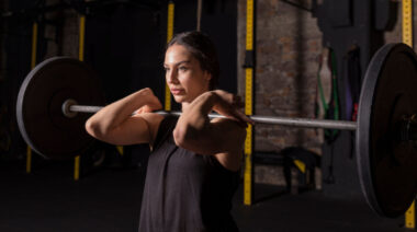 Long-haired person in dark gym holding barbell