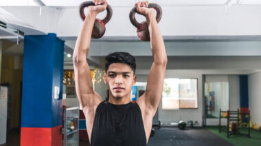 Person in gym pressing two kettlebells overhead