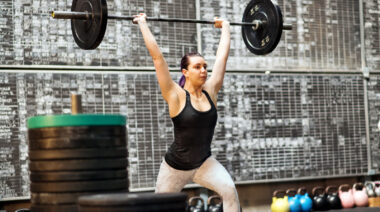 long-haired person in gym lifting barbell overhead