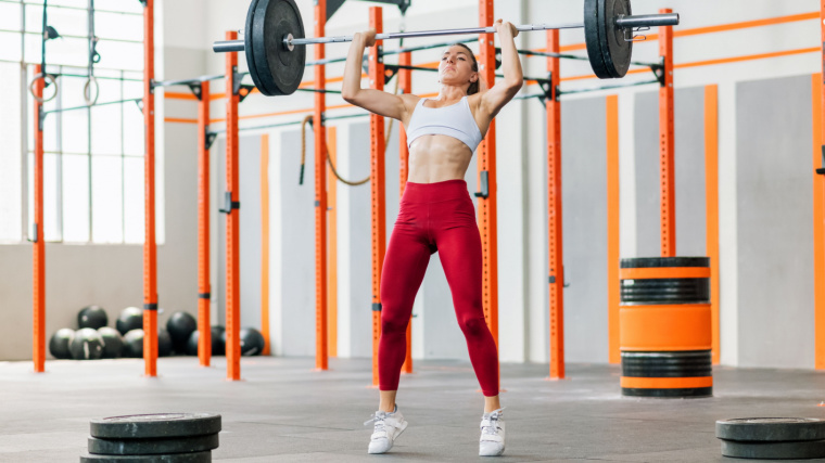 Muscular person in gym pressing barbell overhead