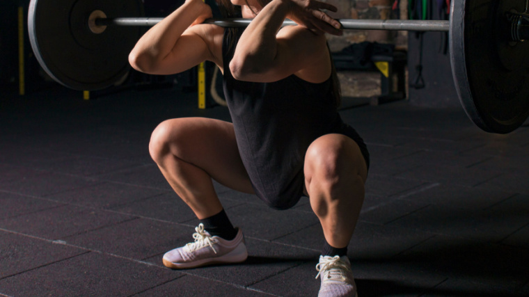 Person in dark gym doing front squat with barbell