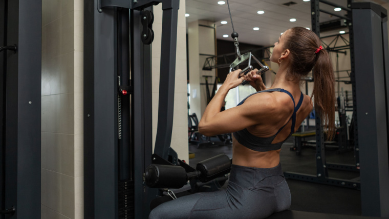 Long-haired person in gym doing lat pulldown