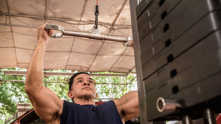 Muscular person in gym lifting weight with lat pulldown exercise