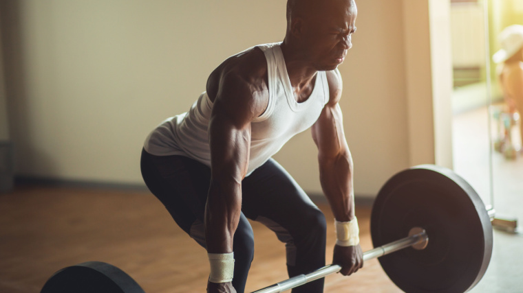 Bald person in gym doing barbell deadlift