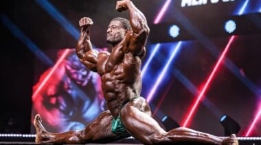 Bodybuilder Andrew Jacked flexing on stage in full split.