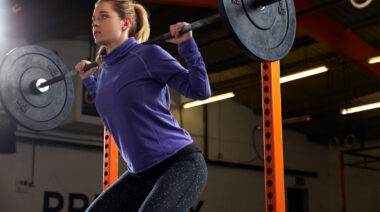 Long-haired person in gym doing barbell squat