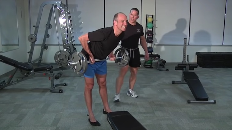 person in gym doing barbell row with personal trainer