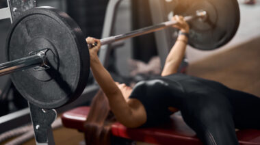 Long-haired person in gym doing barbell bench press