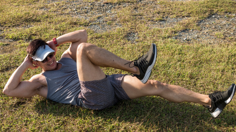 Muscular person outdoors in grass performing bicycle crunch