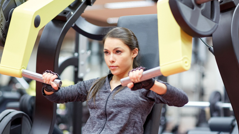 Long-haired person in gym using chest press machine