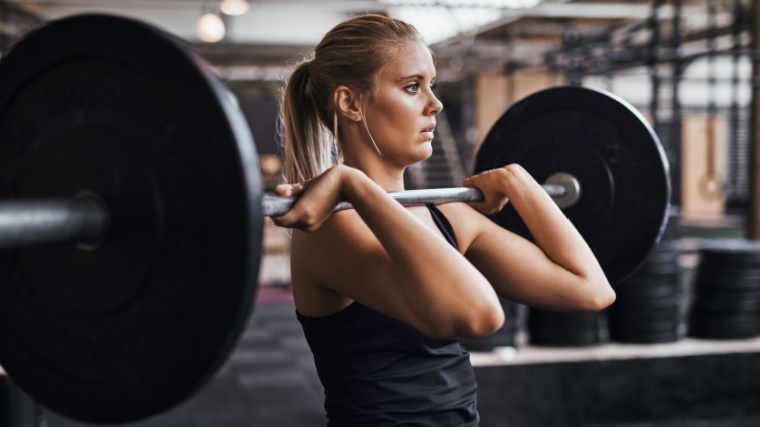 Long-haired person in gym holding barbell for front squat