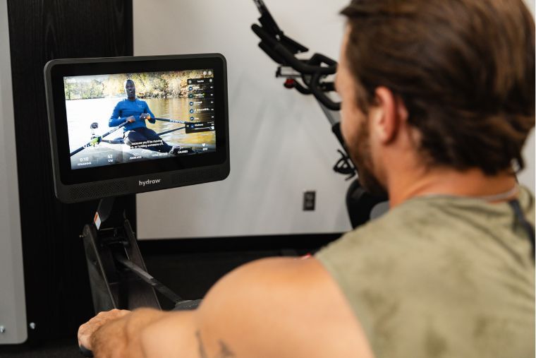 An athlete using the Hydrow Wave with an instructor-led class on the monitor in the background